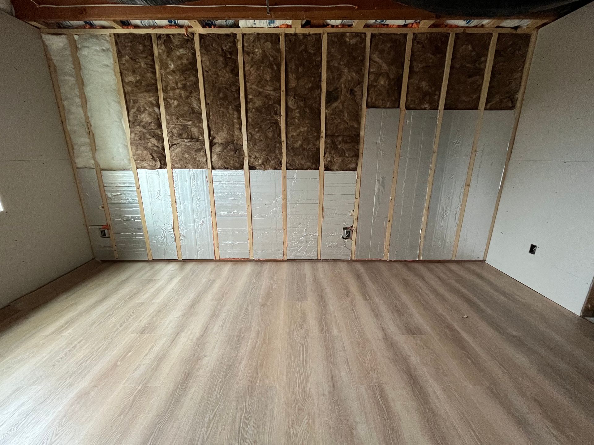 Unfinished room with exposed wall studs, insulation, and a light wood floor.