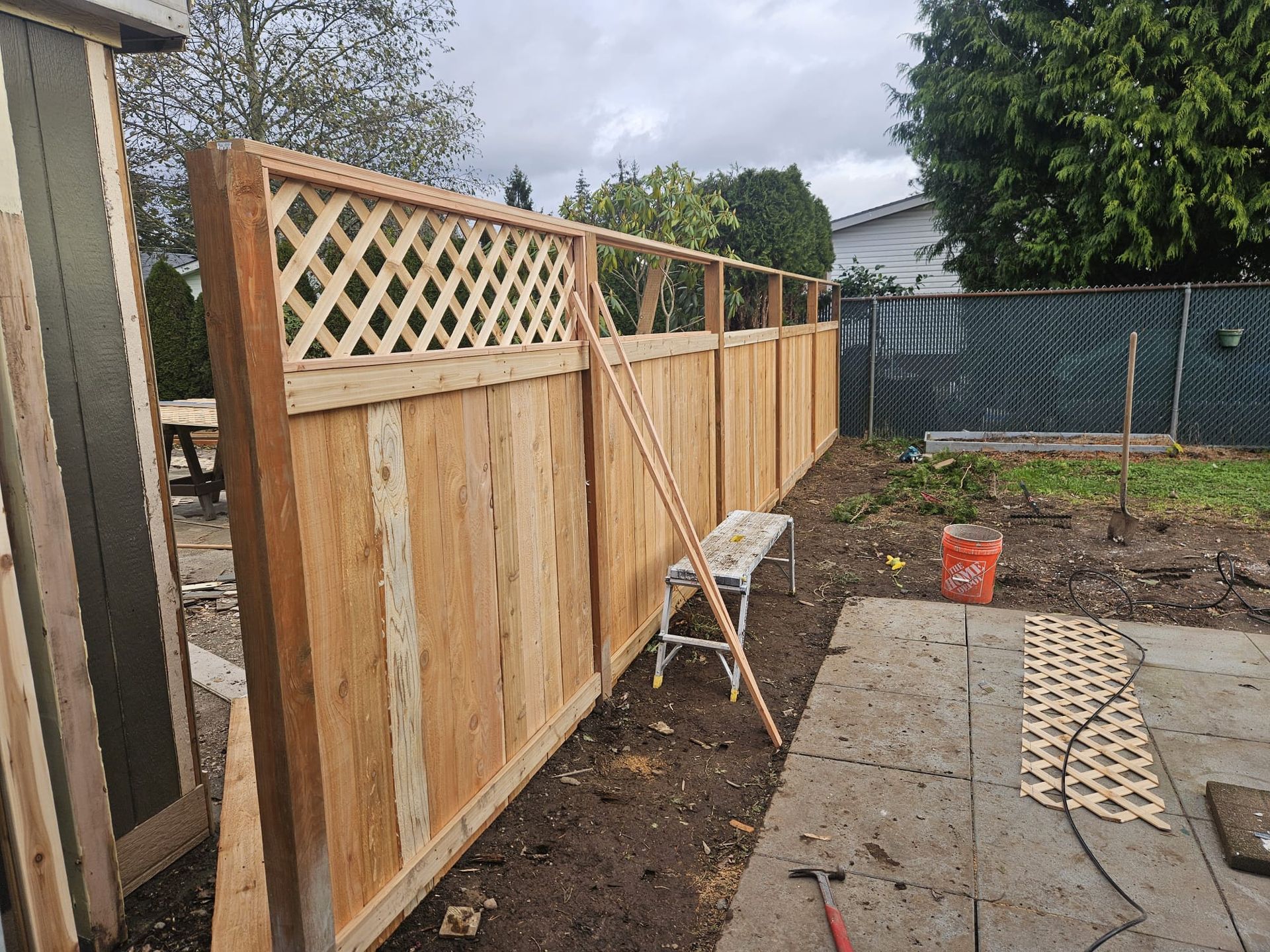 Wooden privacy fence under construction beside a backyard patio, with tools and lattice panels visible.