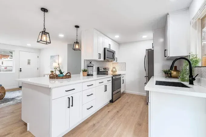 Bright modern white kitchen with island, pendant lights, black fixtures, and wood floors