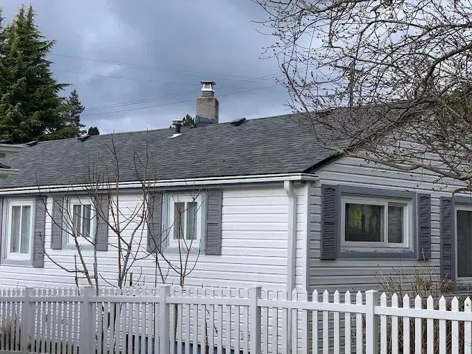 White single-story house with gray roof and picket fence under a cloudy sky.