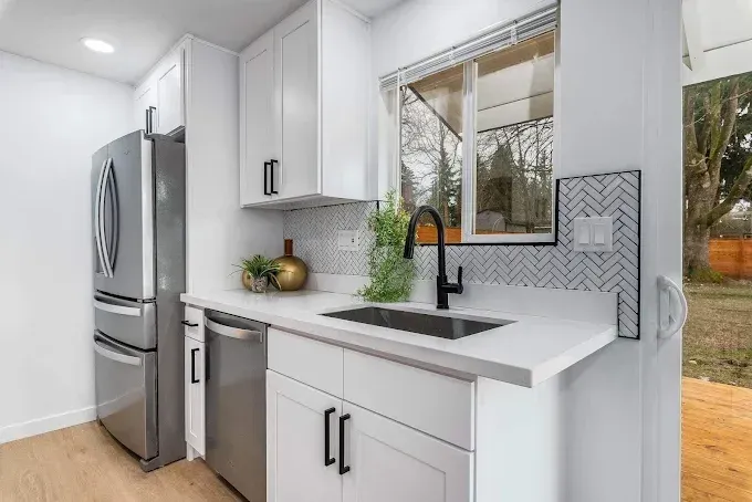 Modern white kitchen with stainless steel fridge, black sink, and window above the counter