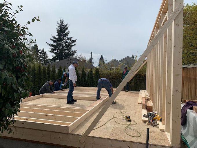 Workers framing a wooden deck on a house construction site, with lumber and tools on the platform.