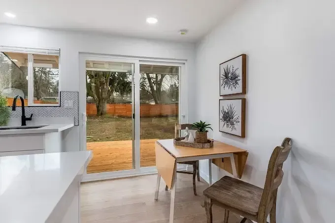 Bright dining nook with sliding glass doors, wooden table, and view of backyard trees and lawn