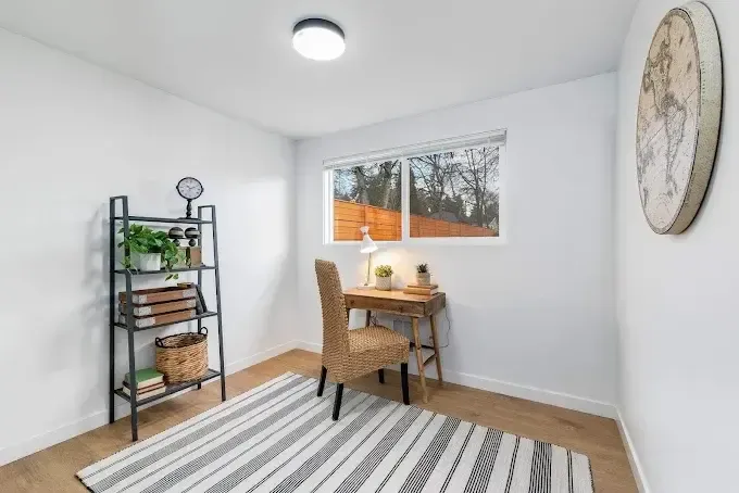 Bright home office with desk, chair, striped rug, shelving, and a window view.