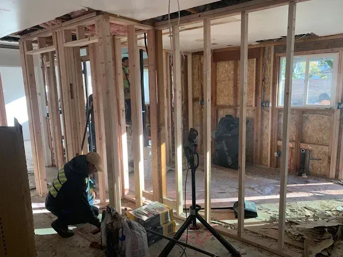 Workers framing a house interior with exposed studs and a window in the background