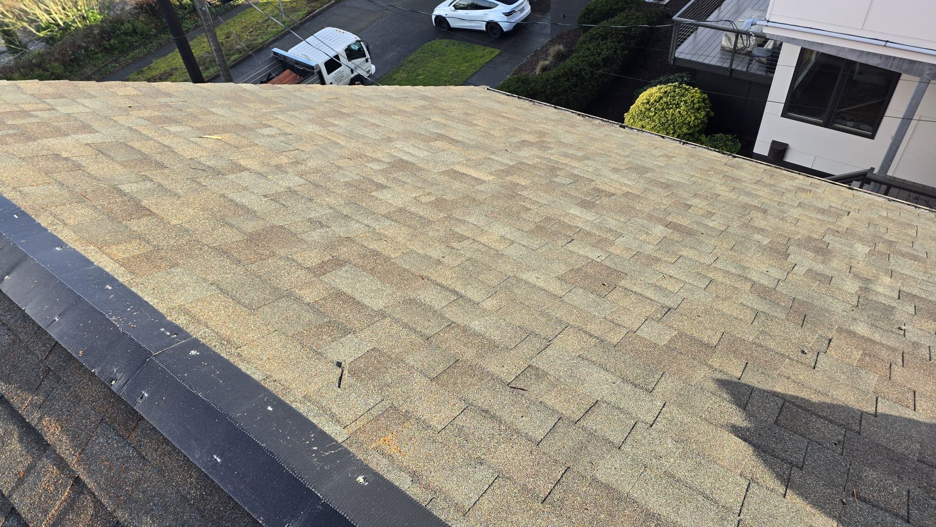 Large tan shingled roof viewed from above, with houses and parked cars visible below.