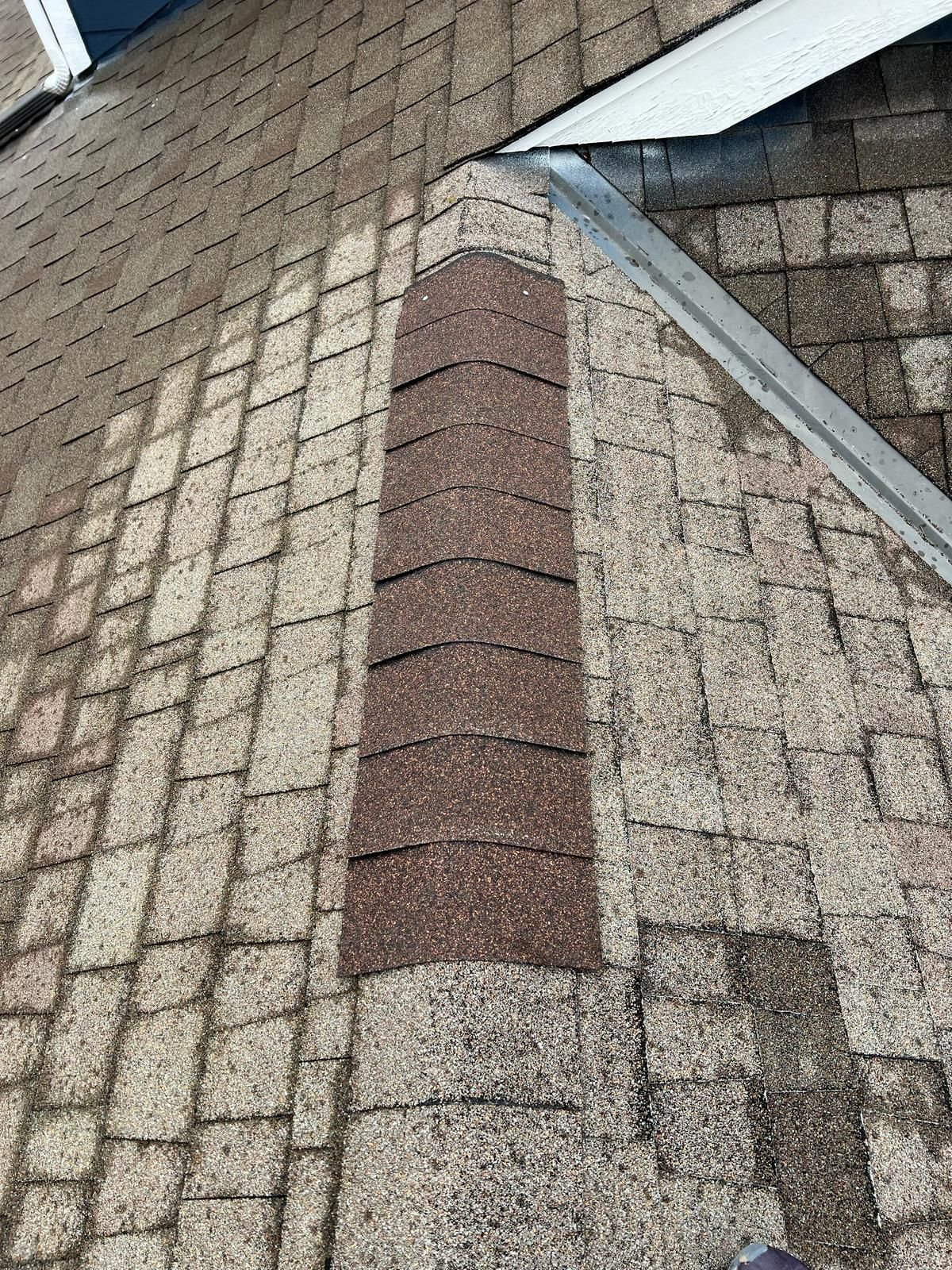 Close-up of a shingled roof with a brown patch of replacement shingles near a ridge vent.