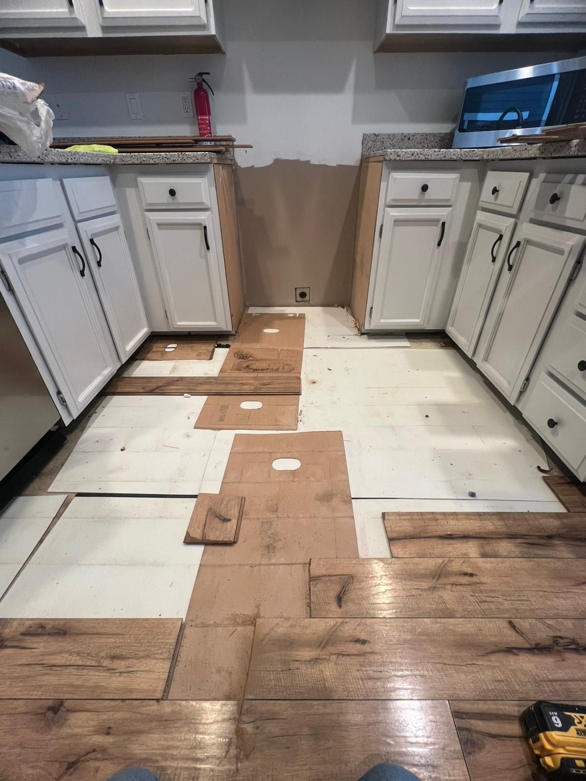 Kitchen with cabinets and a partially removed floor exposing subfloor in the center walkway