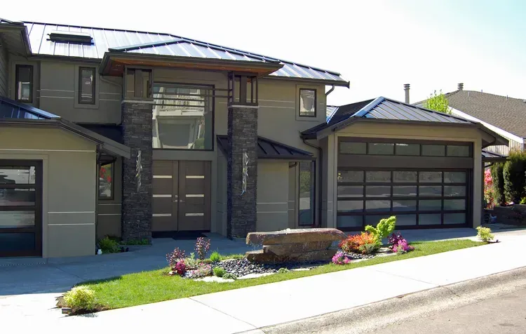 Modern two-story house with a three-car garage and landscaped front yard on a sunny street