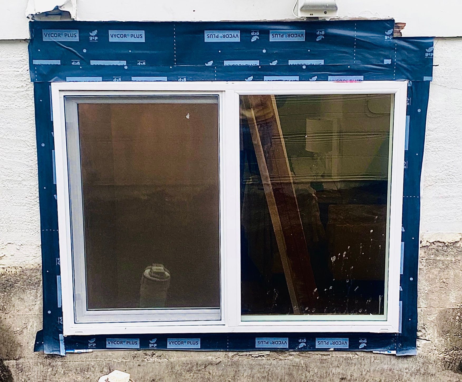 White-framed sliding window installed in a blue protective wrap on an exterior wall