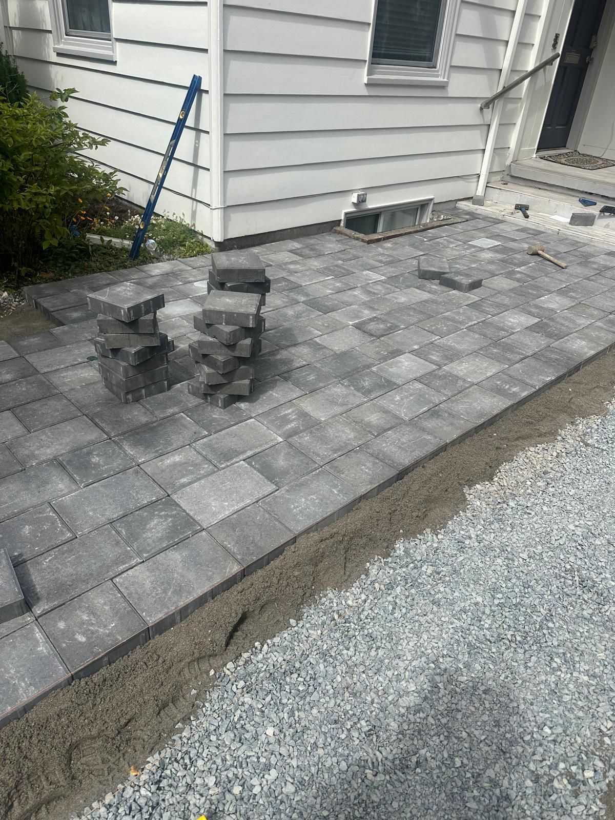Patio under construction with gray pavers, stacked blocks, and house siding along the edge