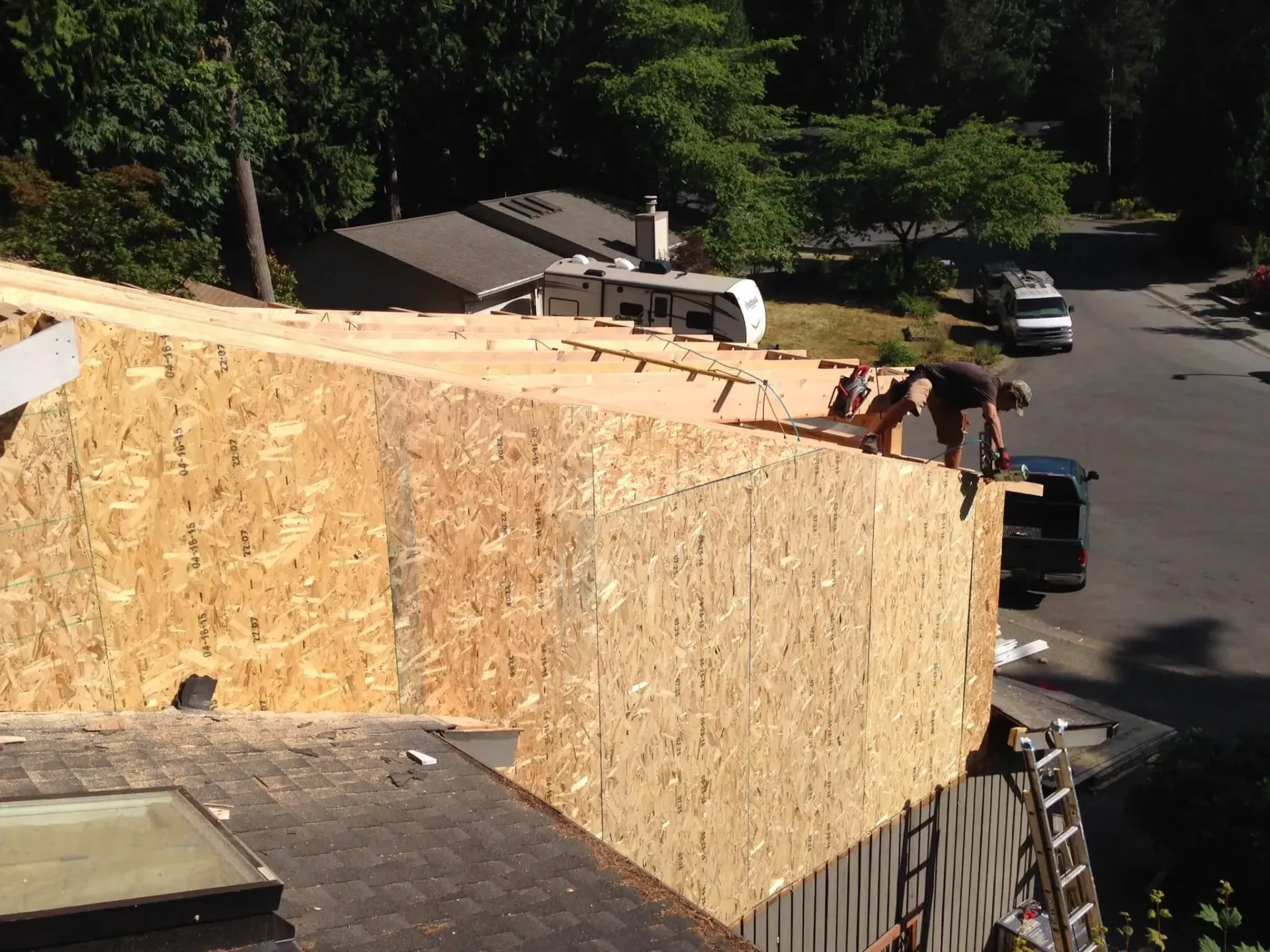 Construction workers atop a plywood wall on a rooftop beside a street and trees