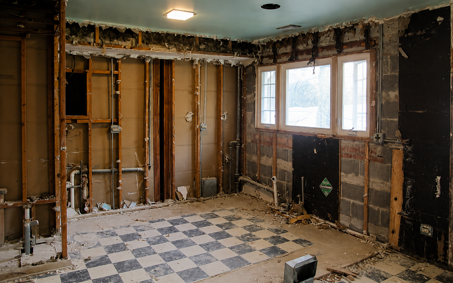Partially demolished kitchen with exposed walls, checkered floor, and windows letting in light