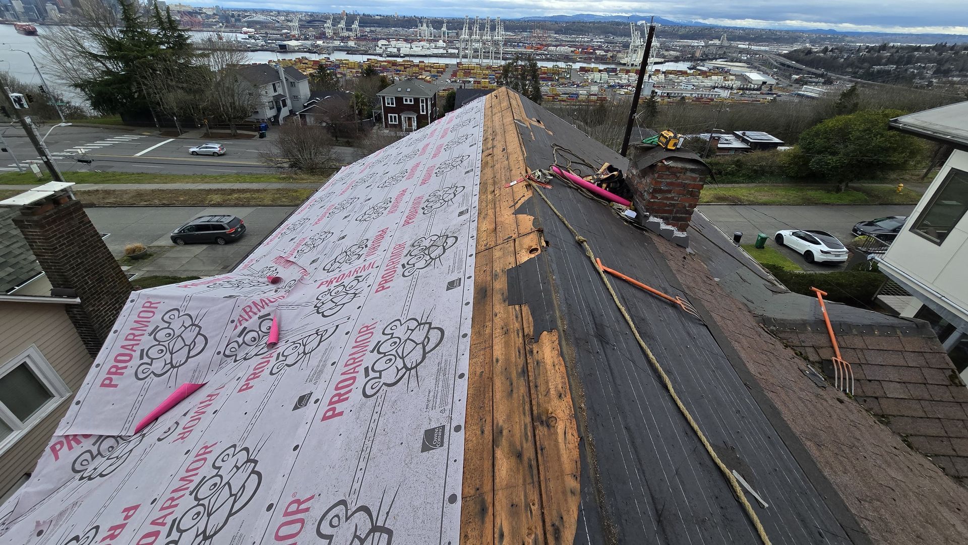 Roofer installing underlayment on a steep roof with city view in the background