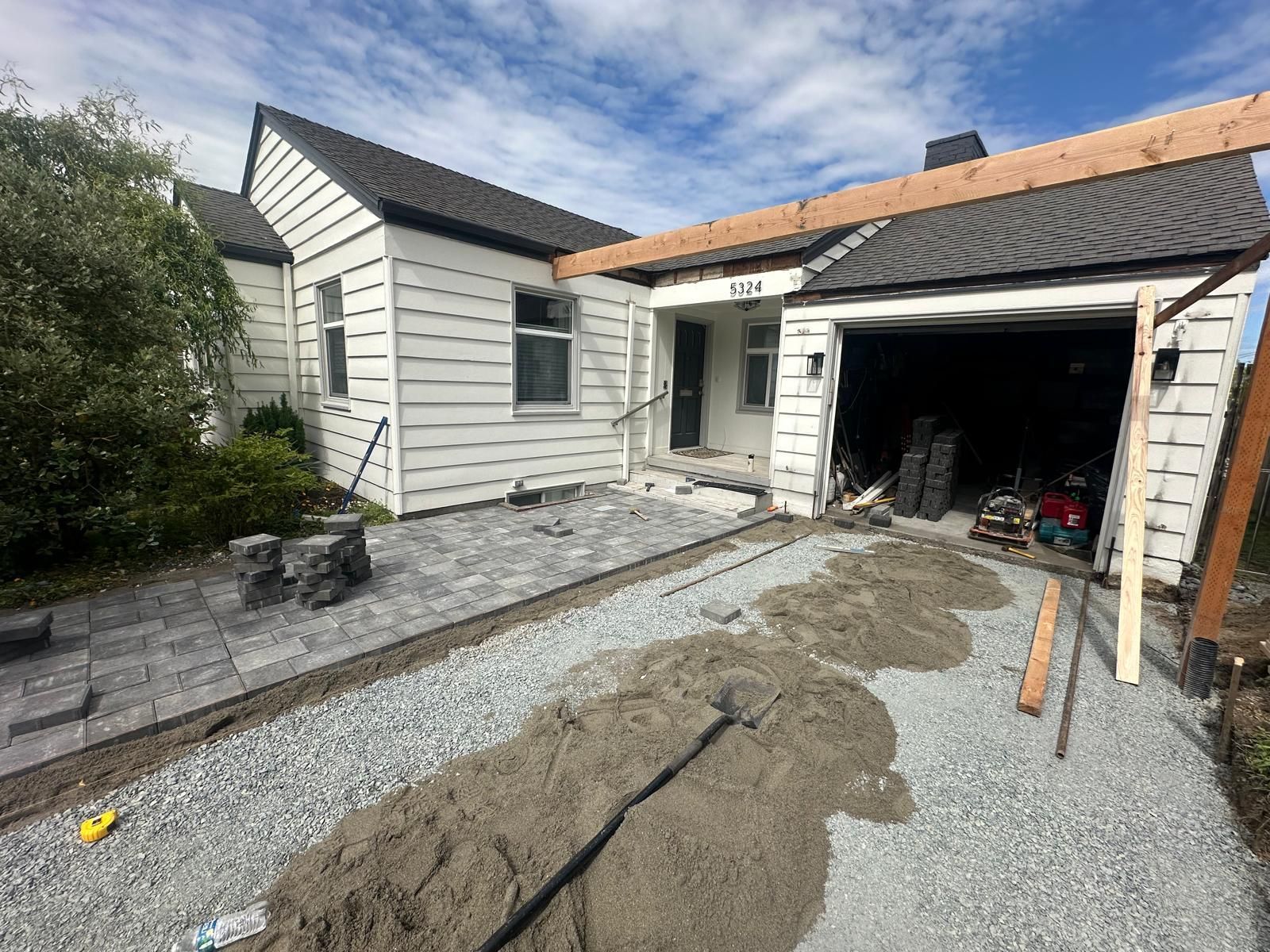 Damaged driveway beside a white house with an open garage and gravel under renovation