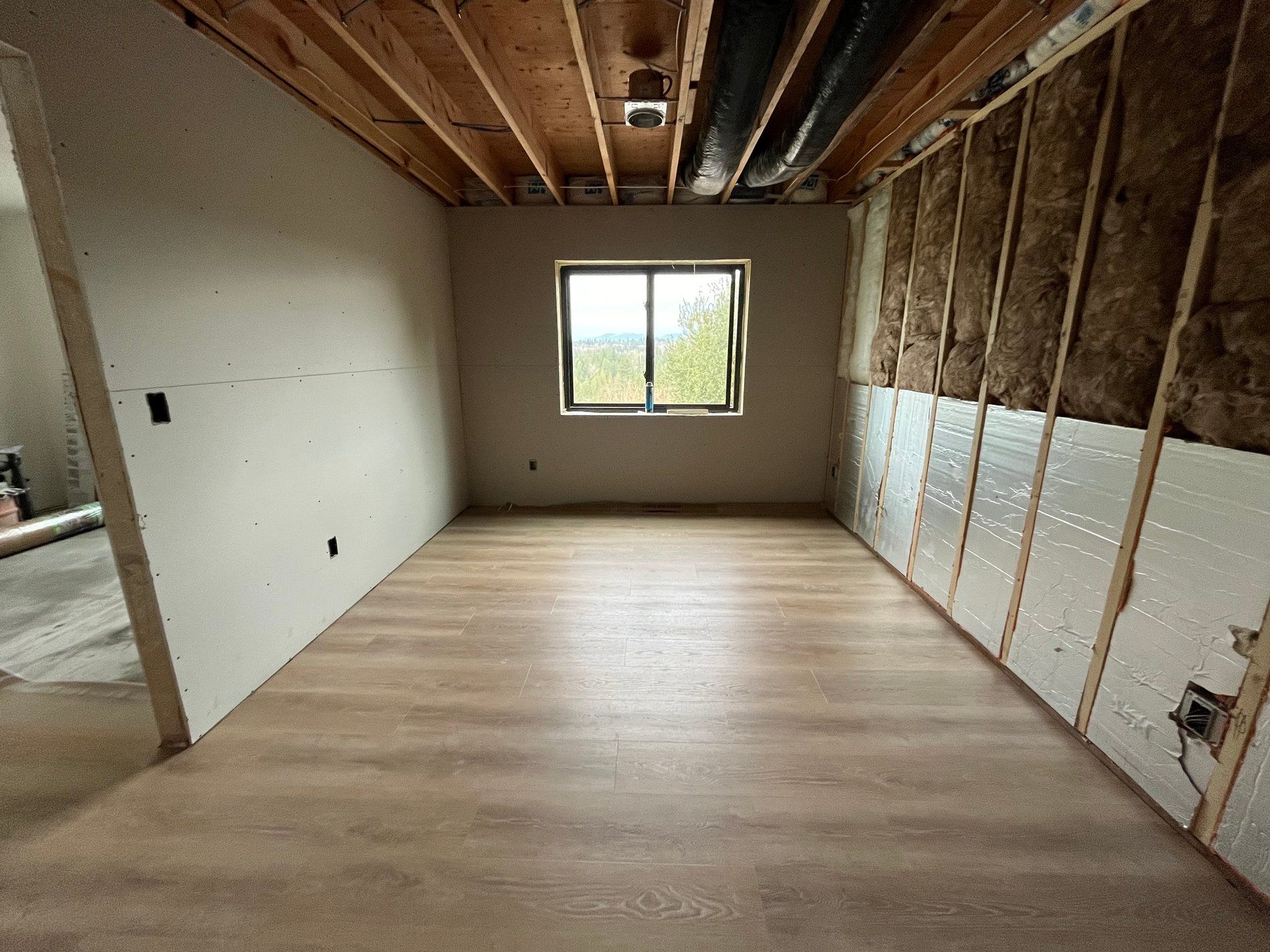 Empty unfinished room with exposed studs, insulation, and a window at the far wall.