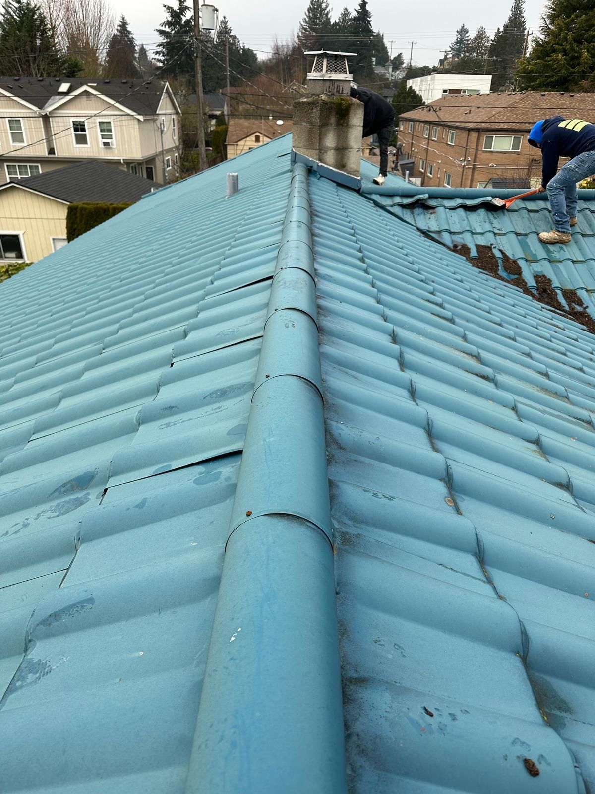 Blue metal roof with a central ridge, viewed from above on an overcast day