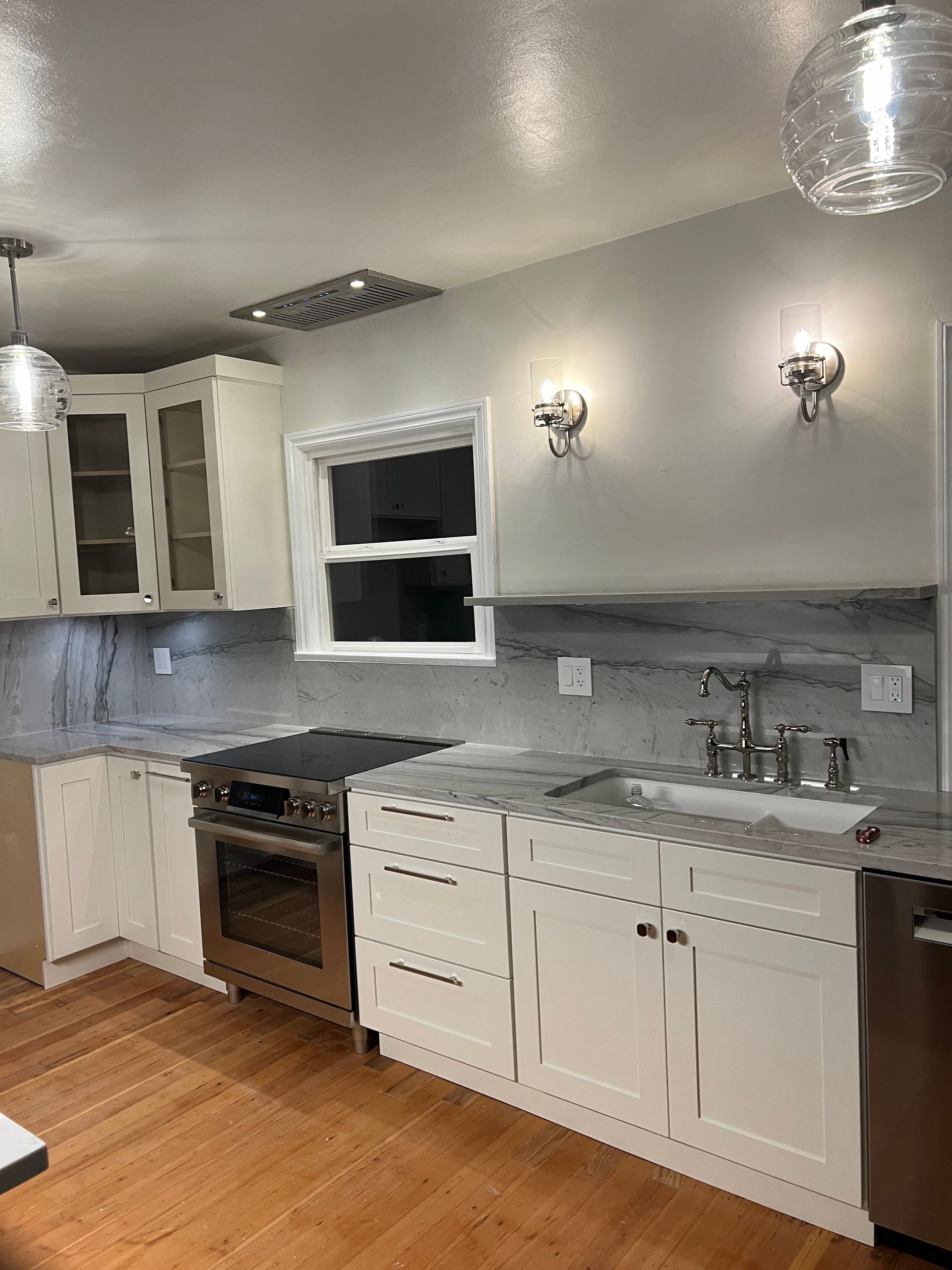 Modern kitchen with white cabinets, gray backsplash, stainless appliances, and hardwood floors