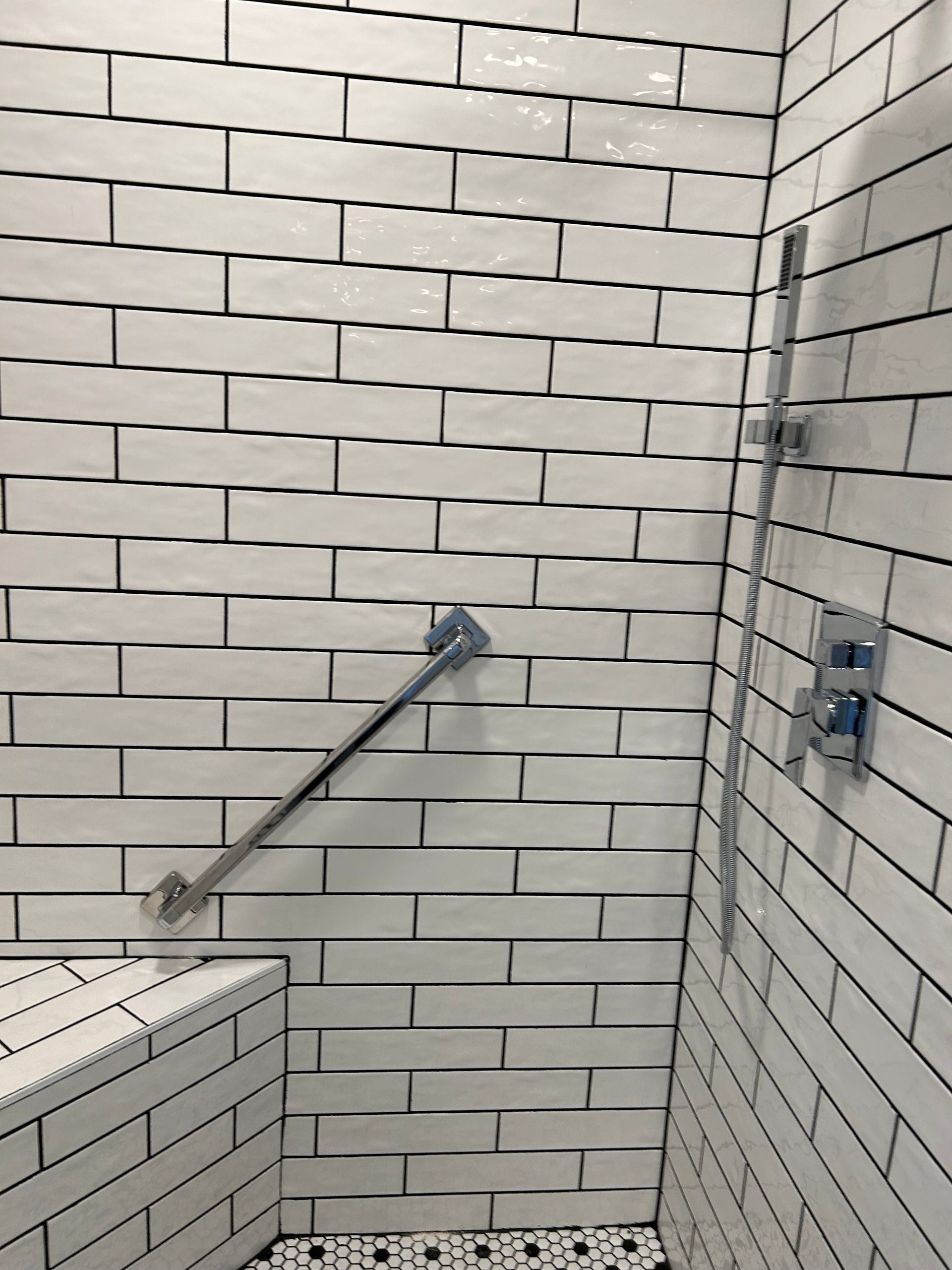 Tile-lined shower corner with a metal grab bar and a bench.
