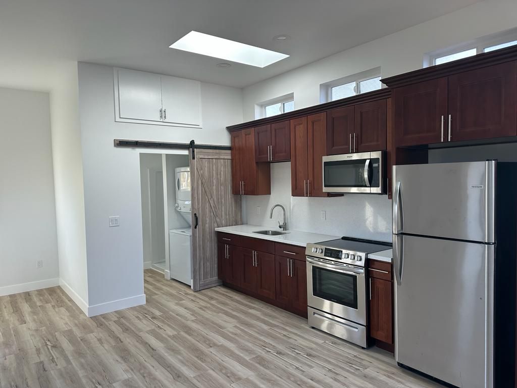 Modern kitchen with stainless steel appliances, dark wood cabinets, and light wood flooring