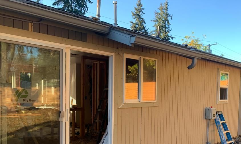 Tan house exterior with open doorway, window, and blue ladder leaning against the wall.