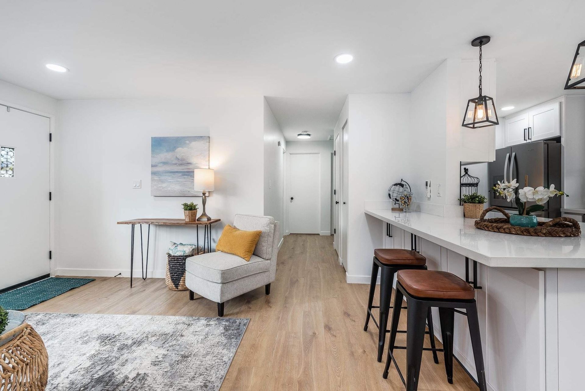 Bright open living room with kitchen bar, gray chair, rug, and white walls