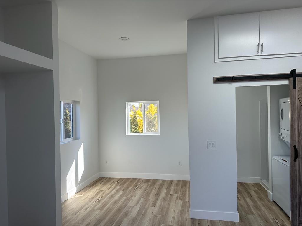 Empty modern room with light wood floors, gray walls, and two small windows letting in daylight