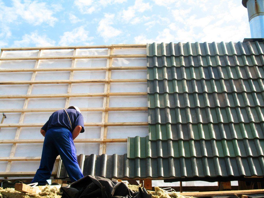 Worker on a roof installing green tiles against a white wall with wooden framing
