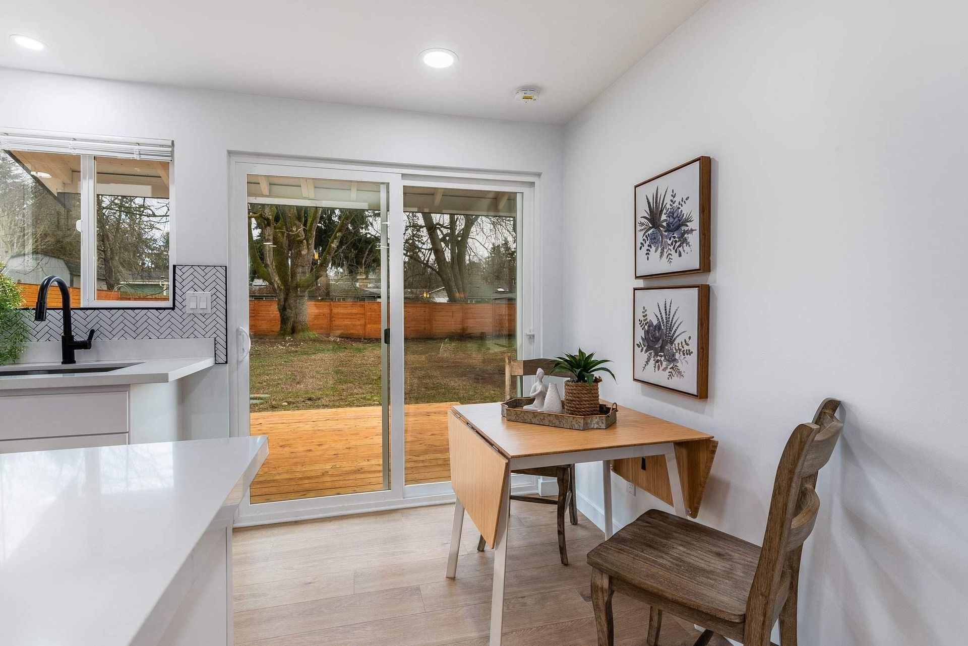 Bright kitchen-dining area with glass sliding doors, white cabinets, wooden table, and chairs overlooking autumn trees