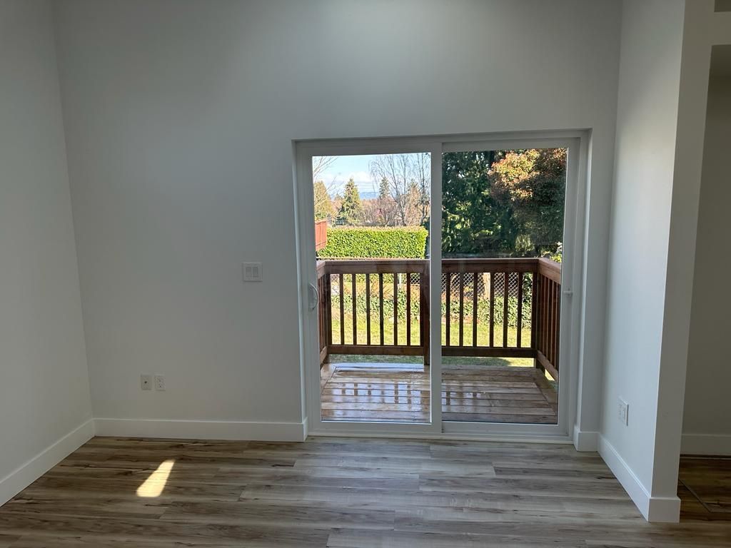 Empty room with wood floor and sliding door opening to a sunlit deck and trees outside