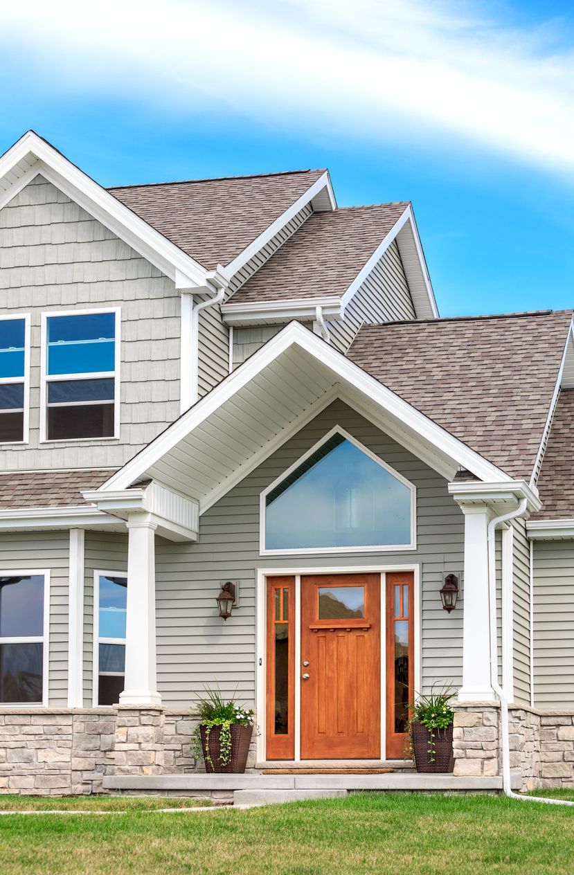 Modern two-story house exterior with gray siding, stone accents, and a wooden front door