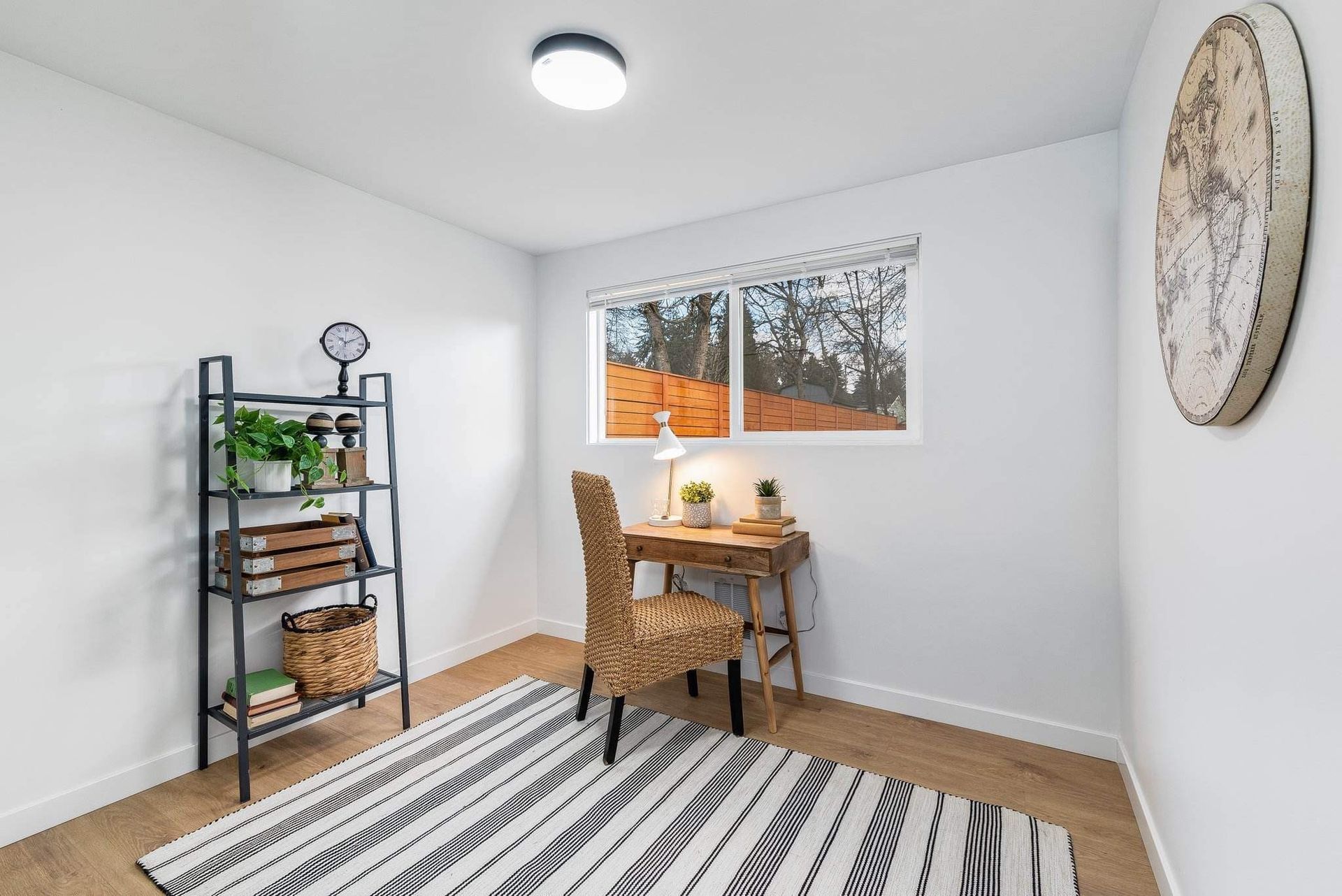 Bright minimalist room with desk, chair, shelving, striped rug, and window view of autumn trees
