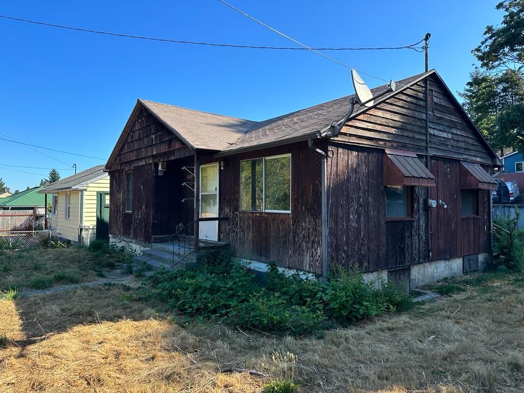 Old weathered wooden house with a metal roof in a dry grassy yard under a clear blue sky