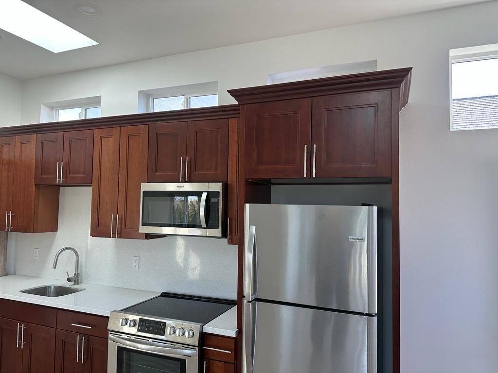 Modern kitchen with dark wood cabinets, stainless steel refrigerator, microwave, and white countertops.
