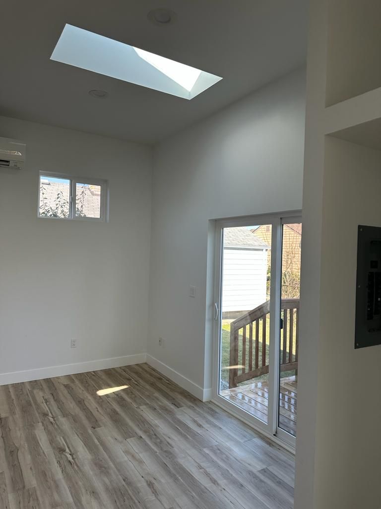Empty bright room with skylight, light wood floors, and sliding glass door to a deck