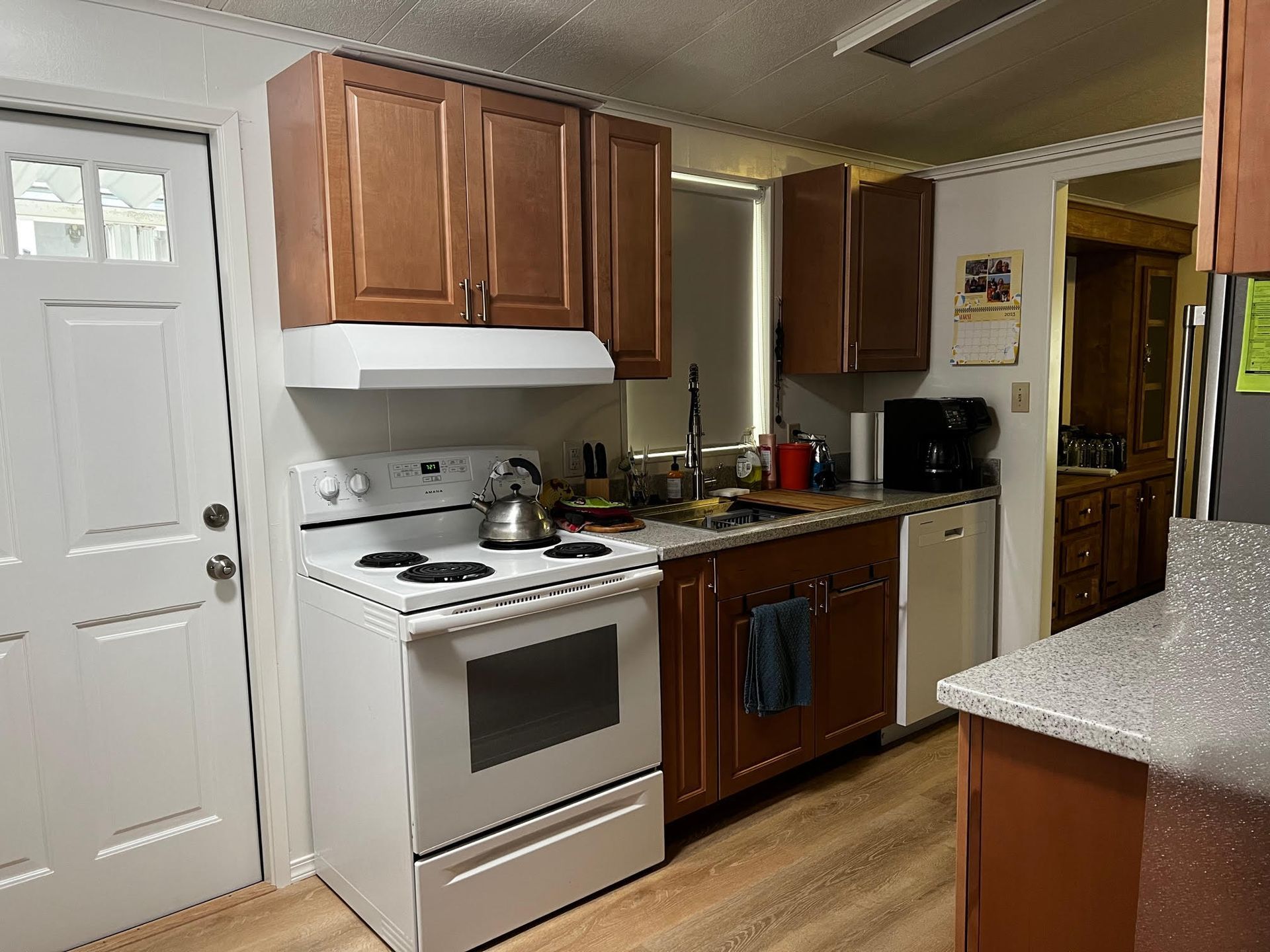 Small kitchen with white stove, wooden cabinets, sink, fridge, and granite countertop