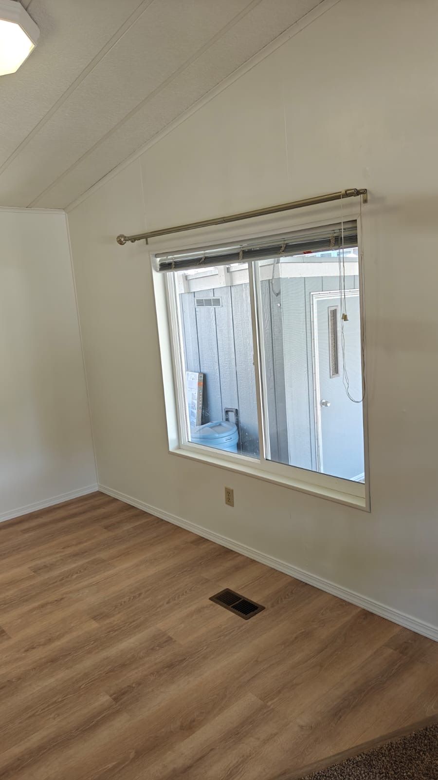 Empty room with wood floor, white walls, and a large window with blinds
