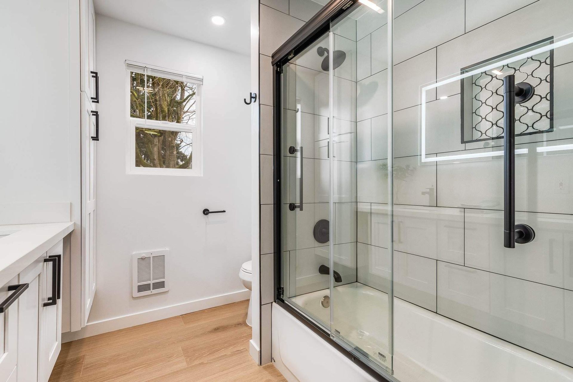 Bright bathroom with white walls, glass shower enclosure, and window near a toilet.