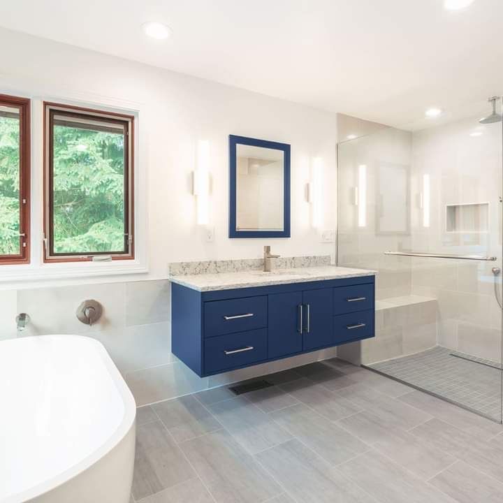 Modern bathroom with navy vanity, mirror, tub, window, and glass shower enclosure