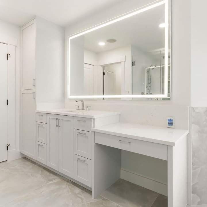 Bright white bathroom vanity with large mirror, sink, cabinets, and built-in makeup desk.