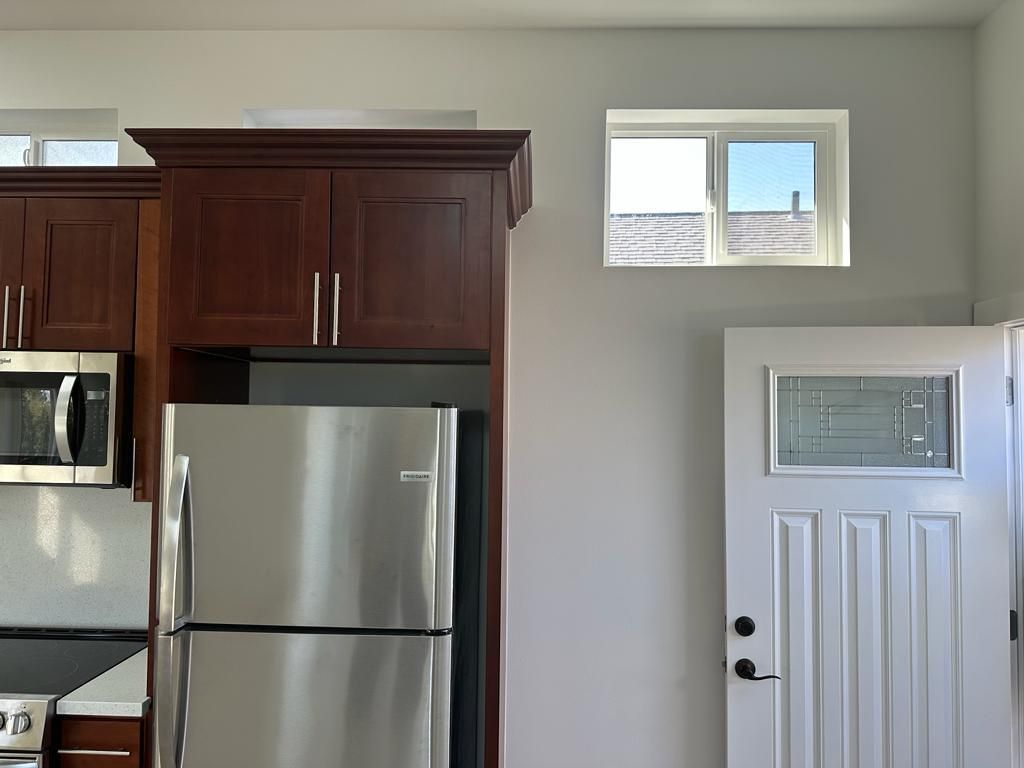 Kitchen with stainless steel refrigerator, dark wood cabinets, and white door with small window above it