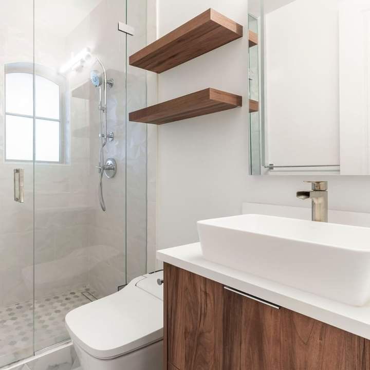 Modern bathroom with glass shower, toilet, wood shelves, and white sink vanity