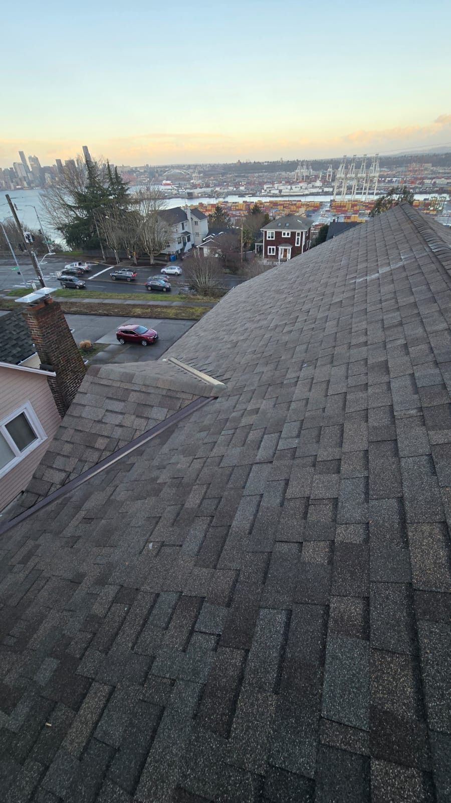 View from a shingled rooftop over a residential neighborhood at sunset, with a parked car below.