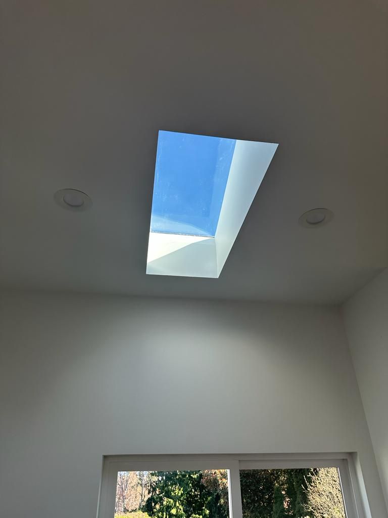 White ceiling with a rectangular skylight showing blue sky above a windowed wall.