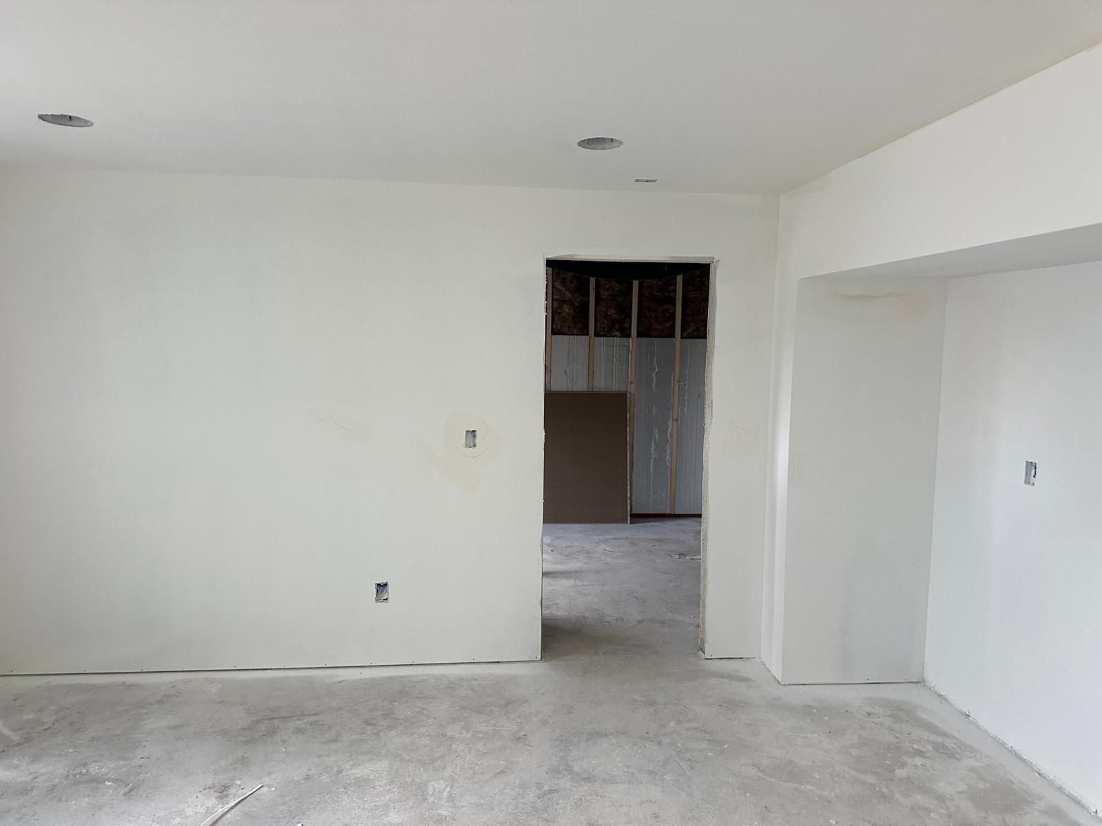Empty white room with bare concrete floor and an open doorway to another unfinished room