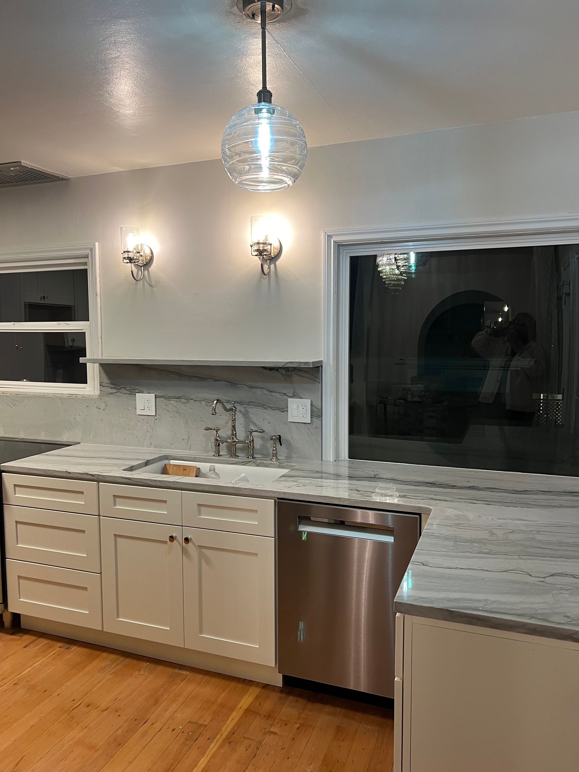 Modern kitchen with gray cabinets, white countertops, stainless dishwasher, and pendant lighting.