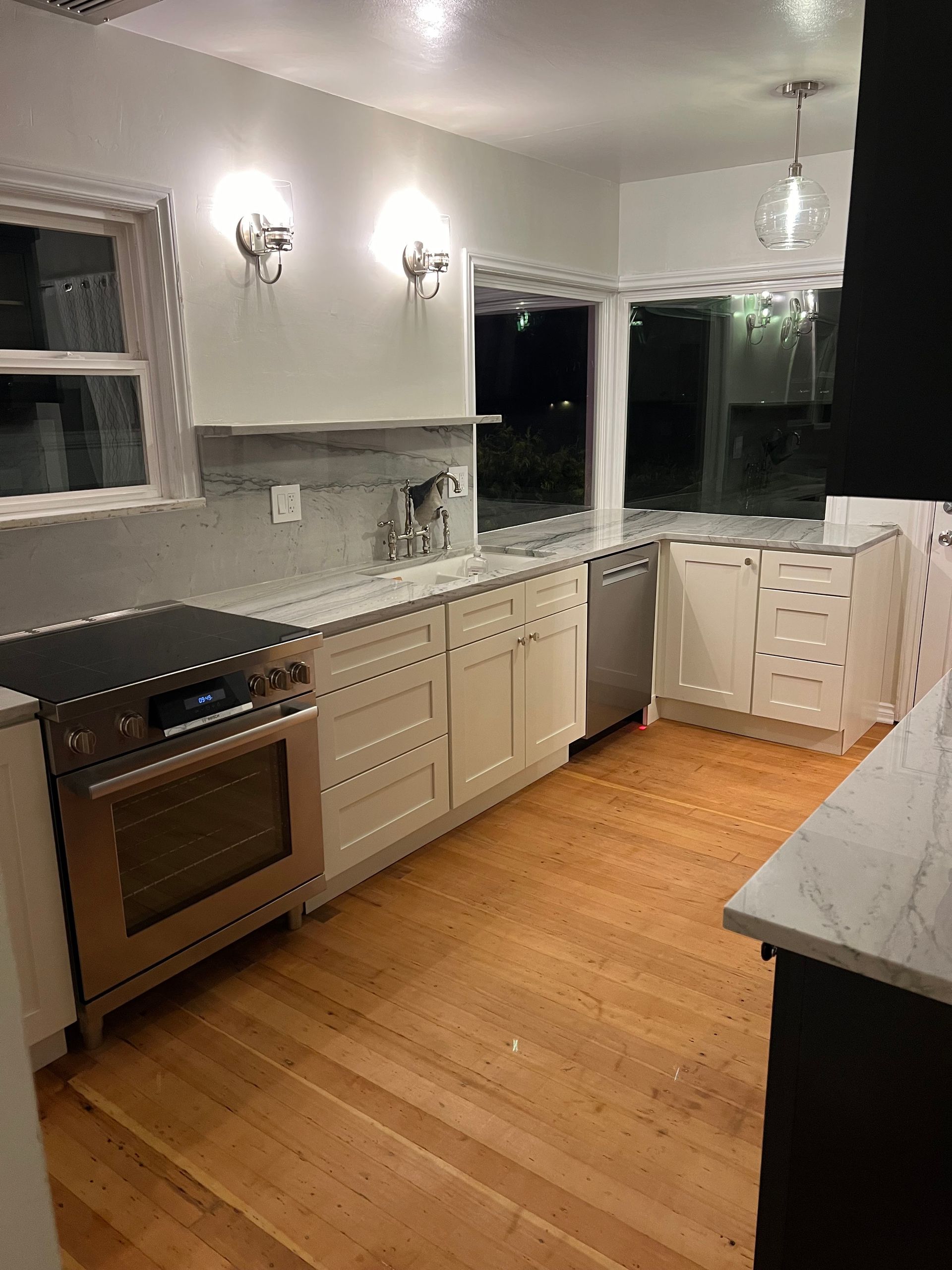 Empty modern kitchen with white cabinets, stainless oven, wood floor, and a gray countertop.