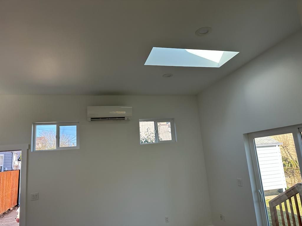 Empty white room with small windows, wall-mounted AC, skylight, and a staircase railing on the right
