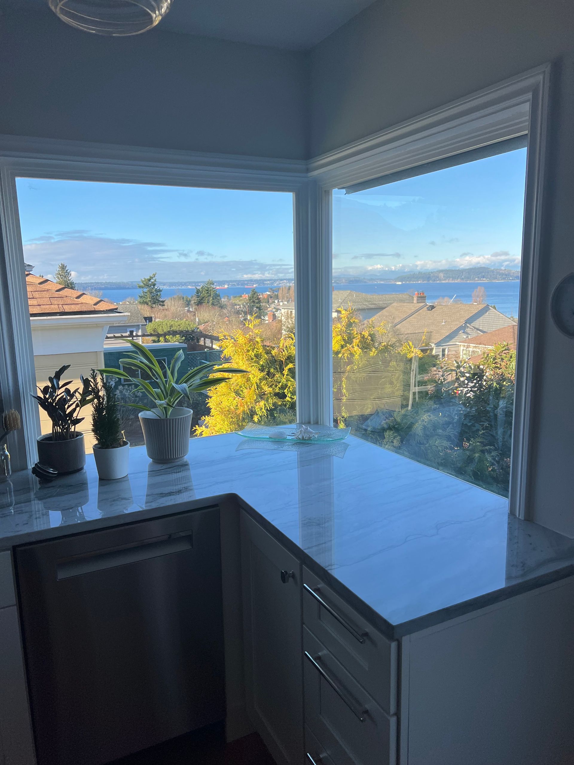 Corner kitchen window with potted plants and a glossy black counter overlooking rooftops and mountains