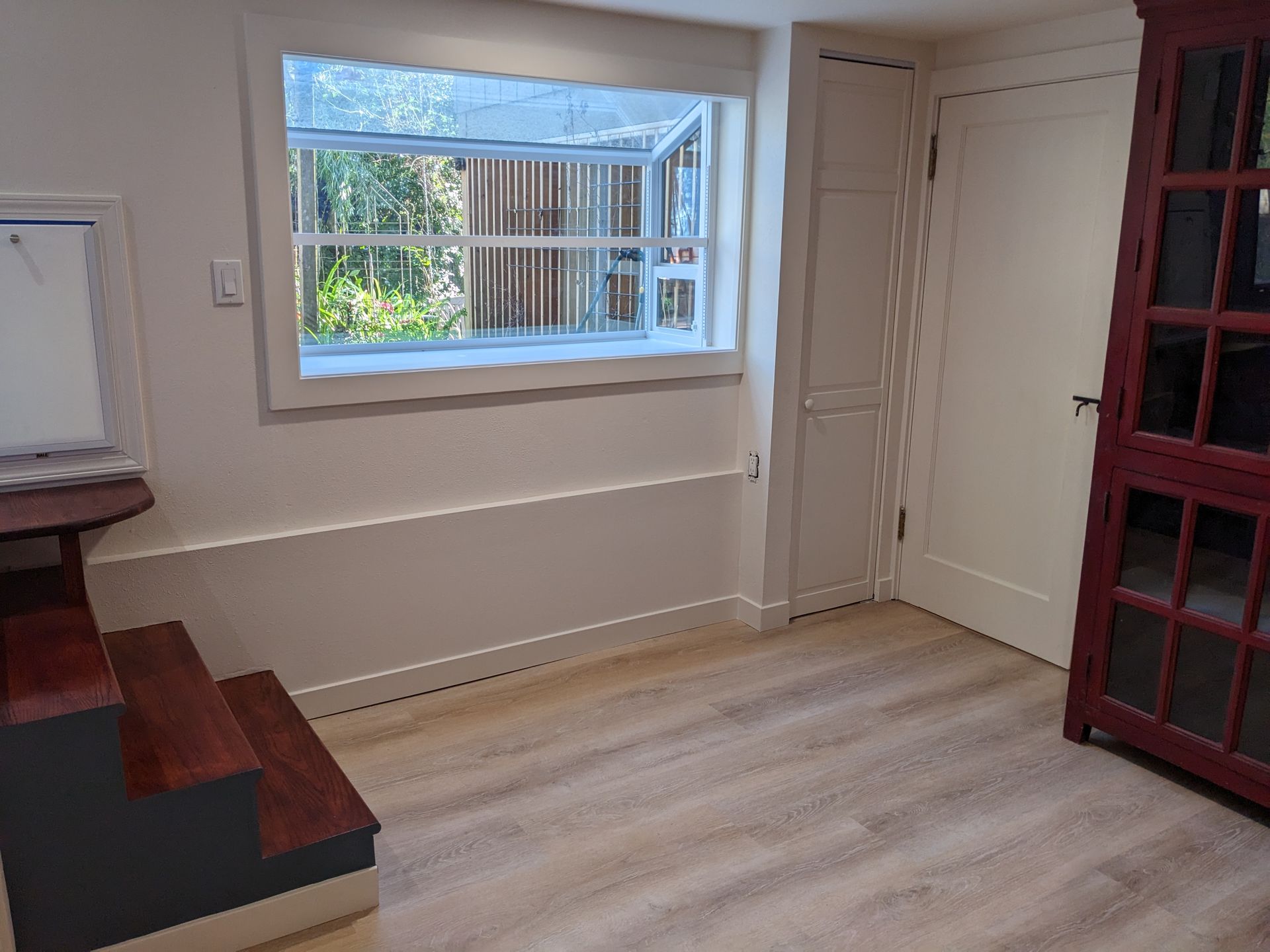 Empty room with wood floor, window, built-in shelves, and white doors.